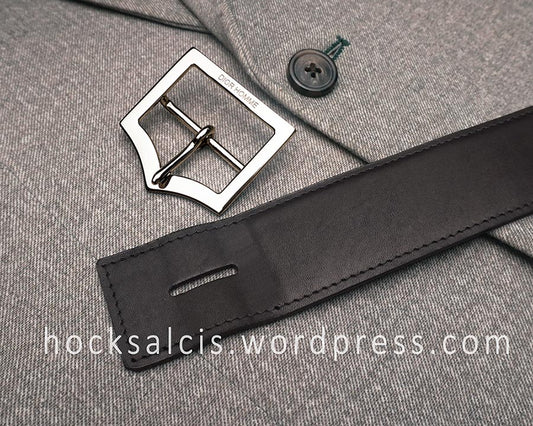 Black replacement leather belt strap next to newly electroplated Dior Homme buckle on a gray fabric background